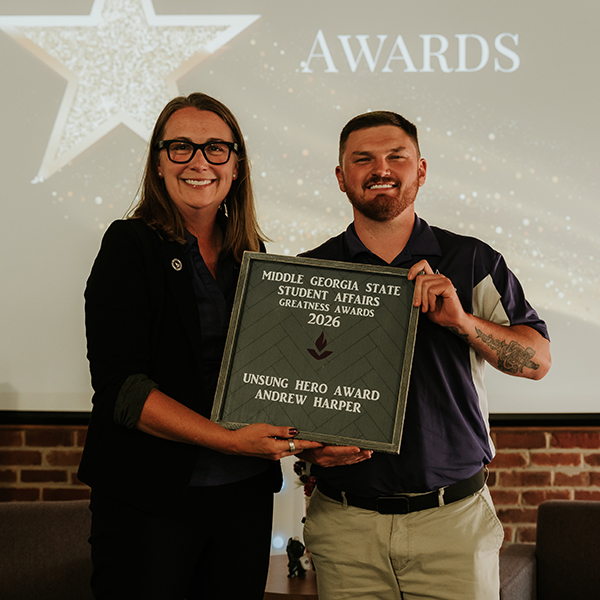 Dr. Jennifer Brannon and award recipient Andrew Harper smile while holding a plaque that reads, "Middle Georgia State Student Affairs Greatness Awards 2026 - Unsung Hero Award, Andrew Harper."
